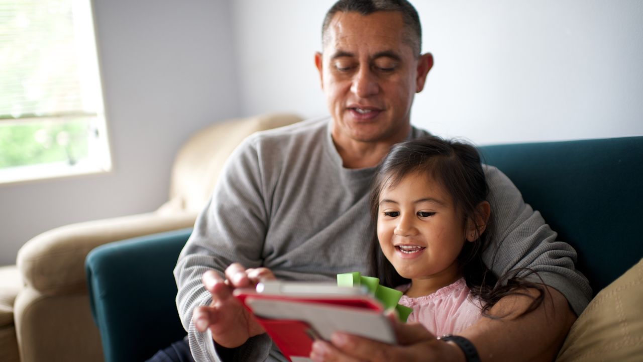 Una niña y su padre leen la Santa Biblia en una tableta