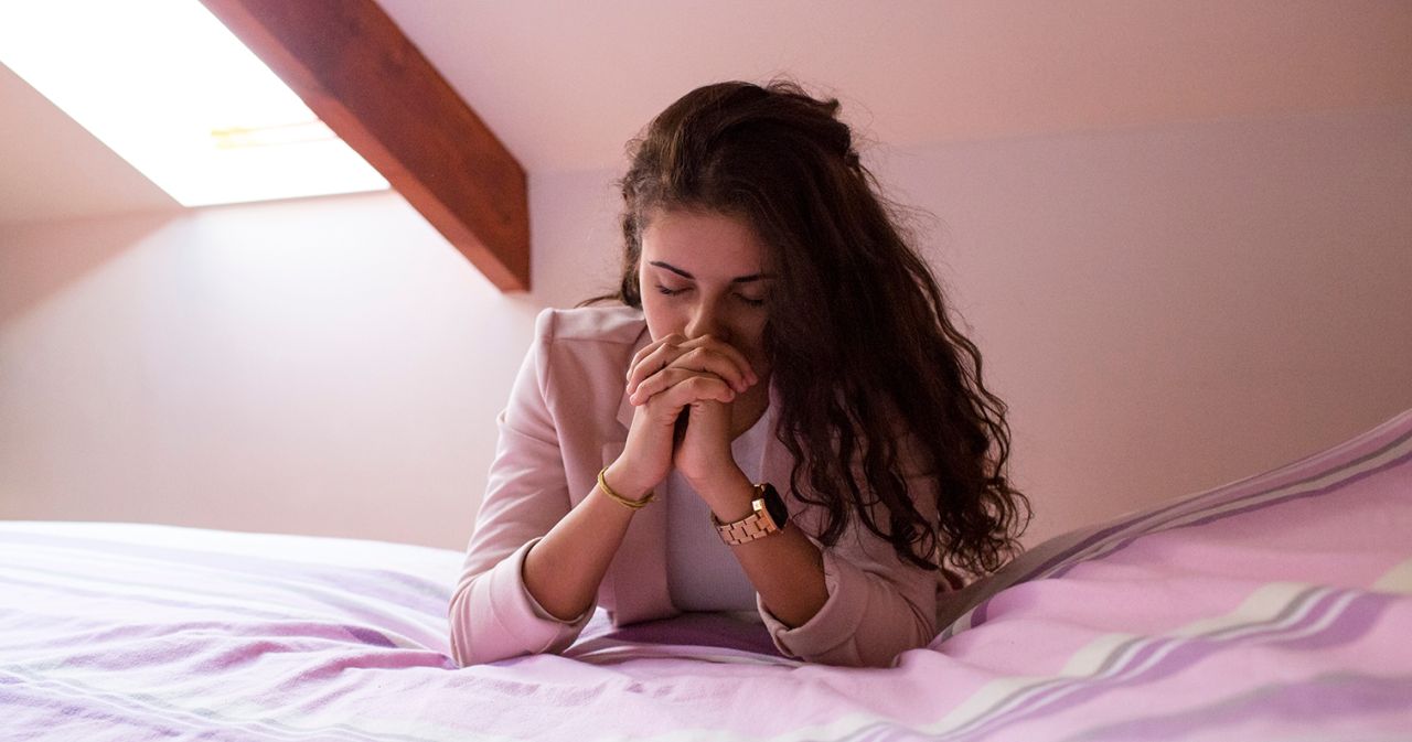 Una mujer orando junto a su cama