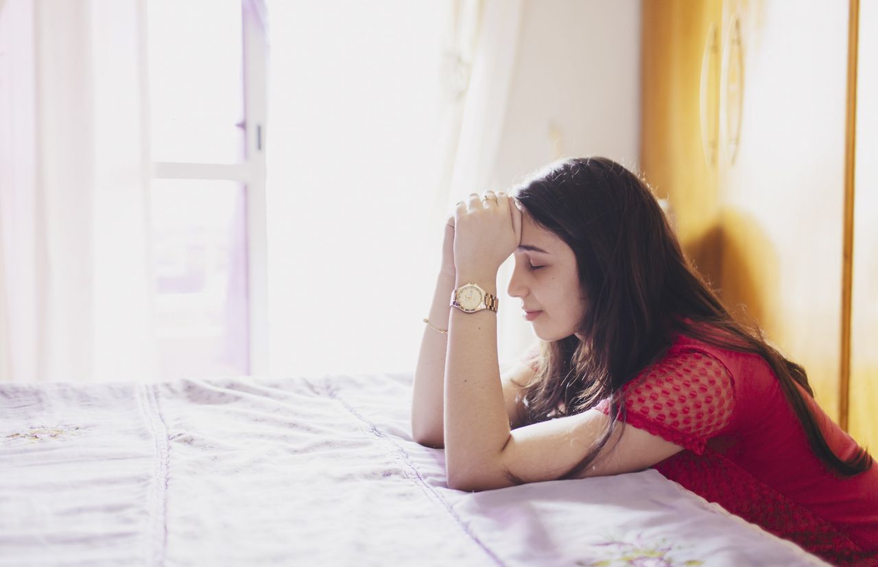 una joven ora junto a su cama